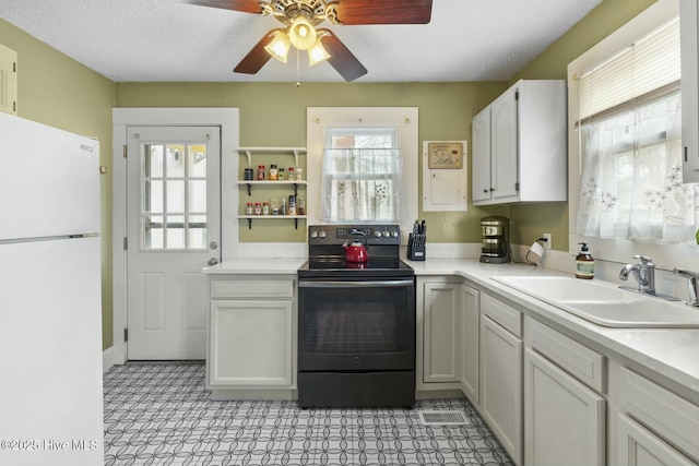 kitchen with black / electric stove, light countertops, a sink, and freestanding refrigerator