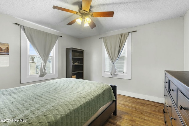 bedroom featuring a ceiling fan, a textured ceiling, baseboards, and wood finished floors