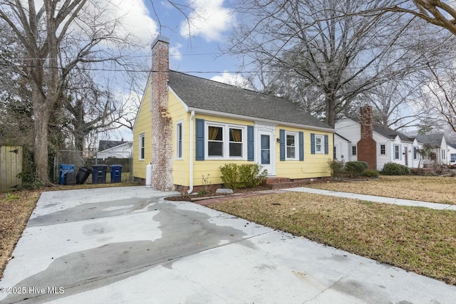 view of front of property featuring a shingled roof, a chimney, a front yard, and fence