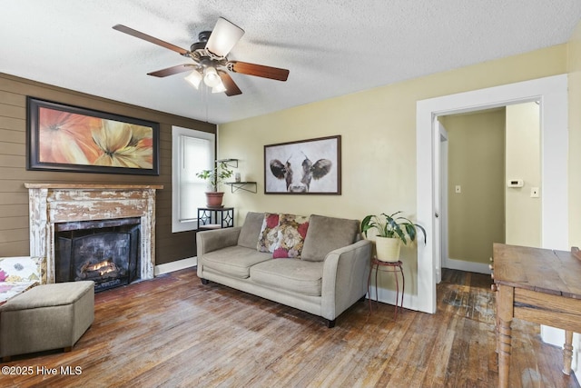 living area with a textured ceiling, a fireplace, wood finished floors, and baseboards