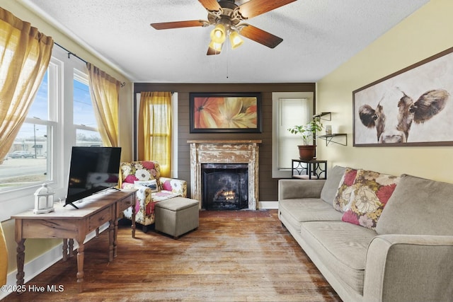 living room featuring ceiling fan, a fireplace, a textured ceiling, and wood finished floors