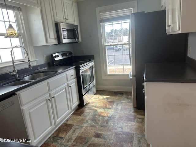 kitchen featuring dark countertops, white cabinetry, stainless steel appliances, and a sink