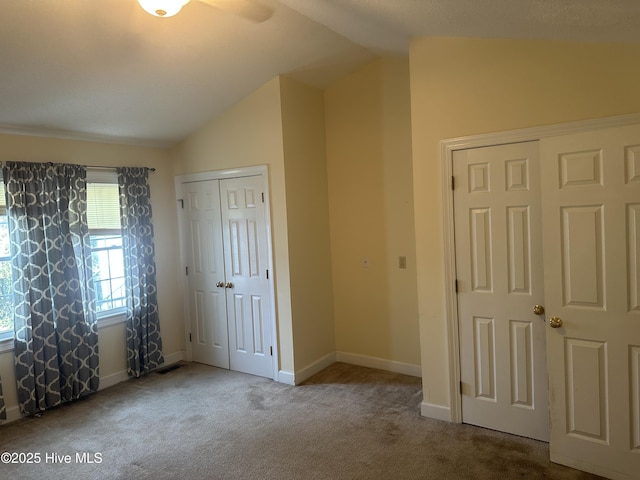 unfurnished bedroom featuring baseboards, vaulted ceiling, a closet, and light colored carpet