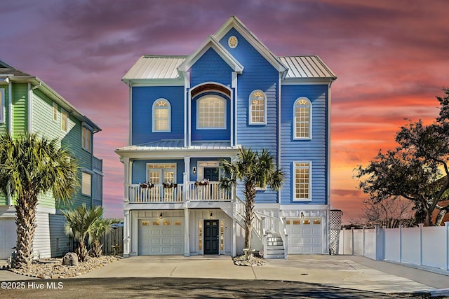 coastal inspired home with a garage, driveway, fence, and metal roof