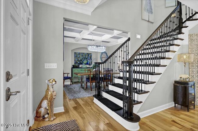 staircase featuring baseboards, coffered ceiling, wood finished floors, and a chandelier