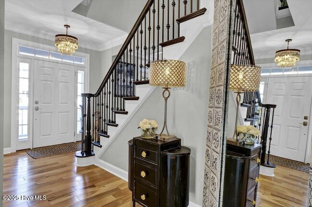 foyer entrance with crown molding, a notable chandelier, light wood-type flooring, baseboards, and stairs