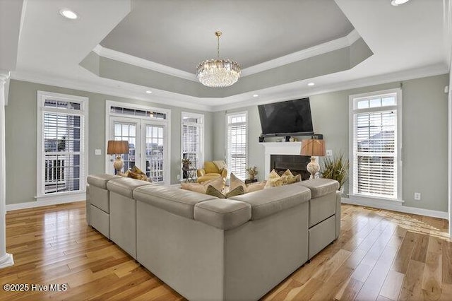 living area featuring a chandelier, light wood-type flooring, a raised ceiling, and a fireplace