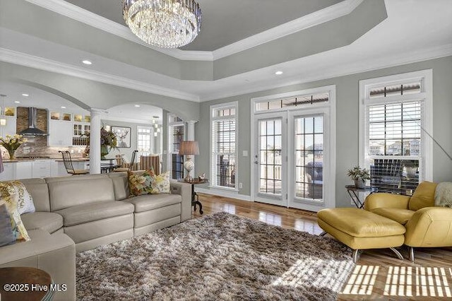 living area featuring a wealth of natural light, a raised ceiling, decorative columns, and an inviting chandelier