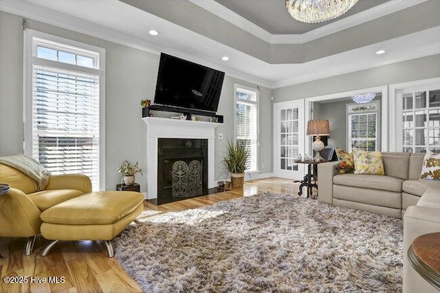 living area featuring a tray ceiling, recessed lighting, ornamental molding, a fireplace with flush hearth, and wood finished floors