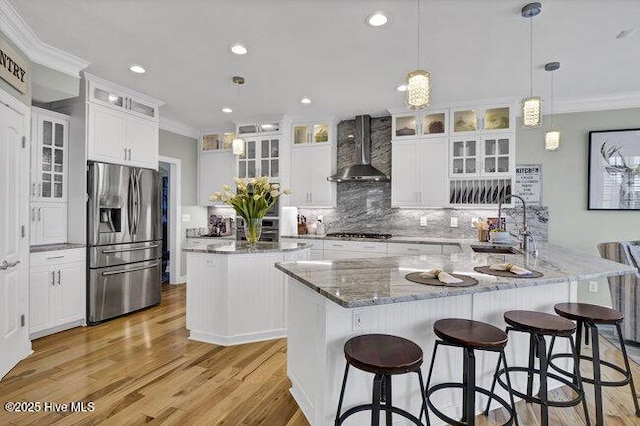 kitchen with a large island, glass insert cabinets, appliances with stainless steel finishes, wall chimney range hood, and white cabinetry