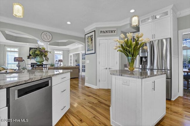 kitchen featuring stainless steel appliances, a kitchen island, white cabinetry, light stone countertops, and glass insert cabinets