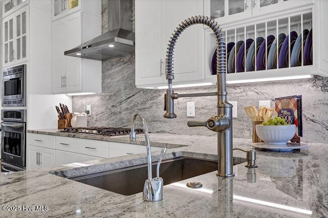 kitchen with glass insert cabinets, white cabinets, stainless steel appliances, and wall chimney range hood