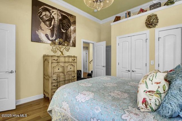 bedroom featuring multiple closets, ornamental molding, wood finished floors, a chandelier, and baseboards