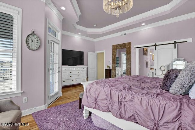 bedroom with a barn door, a raised ceiling, crown molding, and light wood-style flooring