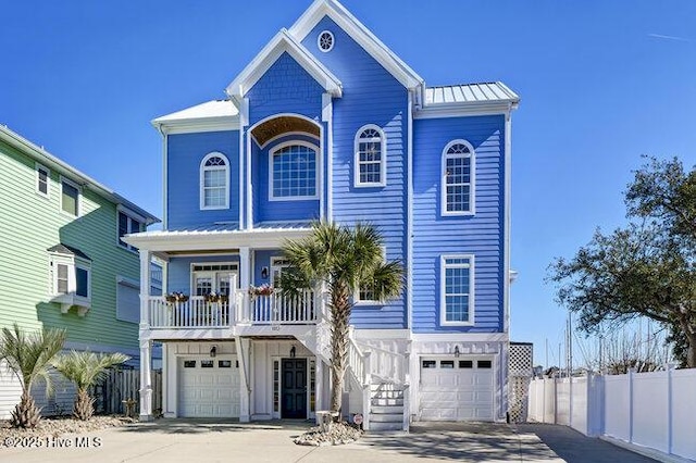 raised beach house with concrete driveway, an attached garage, a standing seam roof, metal roof, and fence