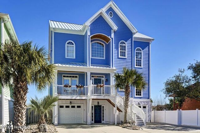 coastal inspired home featuring covered porch, a standing seam roof, fence, metal roof, and a garage