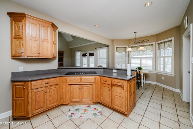 kitchen with brown cabinetry, dark countertops, a peninsula, a wealth of natural light, and light tile patterned flooring