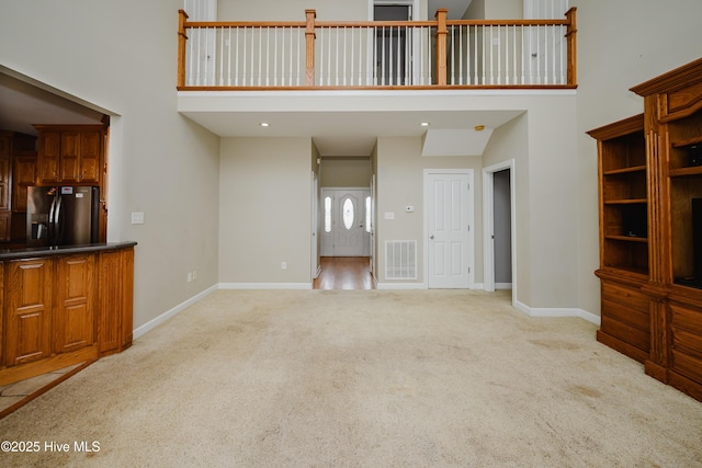 unfurnished living room with recessed lighting, light colored carpet, a towering ceiling, baseboards, and visible vents