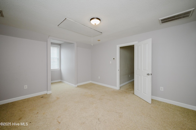 empty room featuring attic access, visible vents, a textured ceiling, and baseboards