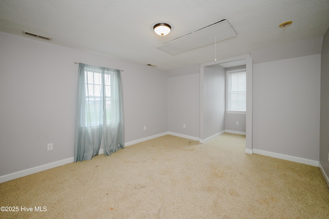 empty room featuring a textured ceiling, plenty of natural light, visible vents, and attic access