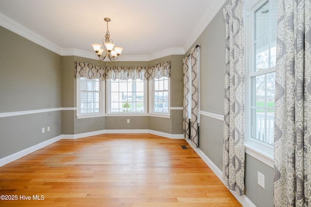 empty room featuring a notable chandelier, ornamental molding, light wood-style flooring, and a healthy amount of sunlight