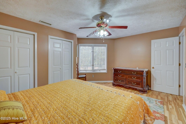 bedroom with visible vents, multiple closets, a ceiling fan, a textured ceiling, and wood finished floors