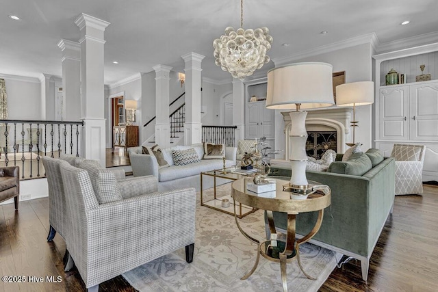 living area featuring a notable chandelier, a fireplace, wood finished floors, ornamental molding, and decorative columns