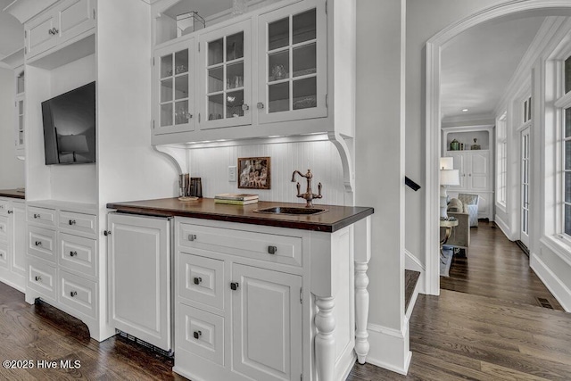 bar featuring baseboards, arched walkways, dark wood finished floors, and a sink