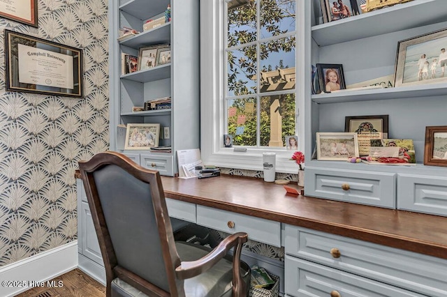 office with wallpapered walls, dark wood-style floors, baseboards, and built in desk