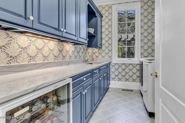 kitchen featuring blue cabinets, wallpapered walls, wine cooler, and a sink