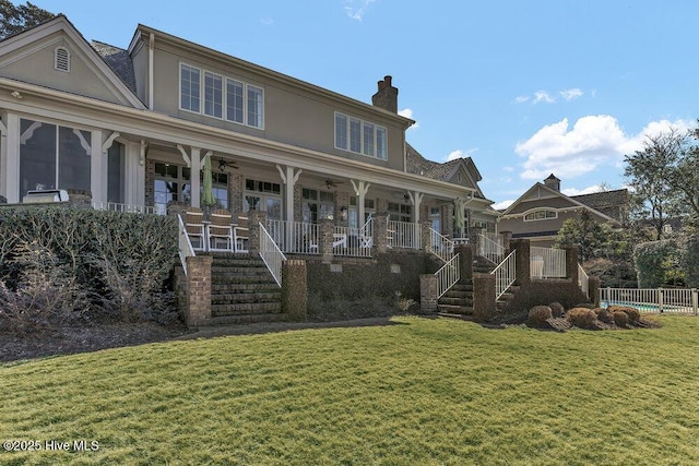 view of front of home with a ceiling fan, a chimney, stairway, covered porch, and a front lawn