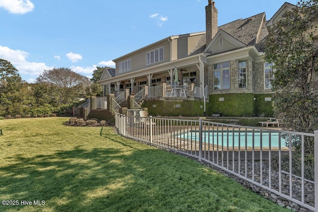 rear view of house with a lawn, a chimney, a community pool, fence, and stucco siding