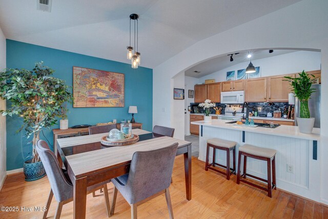 dining room with arched walkways, visible vents, baseboards, vaulted ceiling, and light wood finished floors