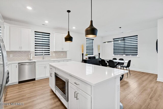 kitchen with stainless steel appliances, light countertops, open floor plan, white cabinets, and wall chimney exhaust hood