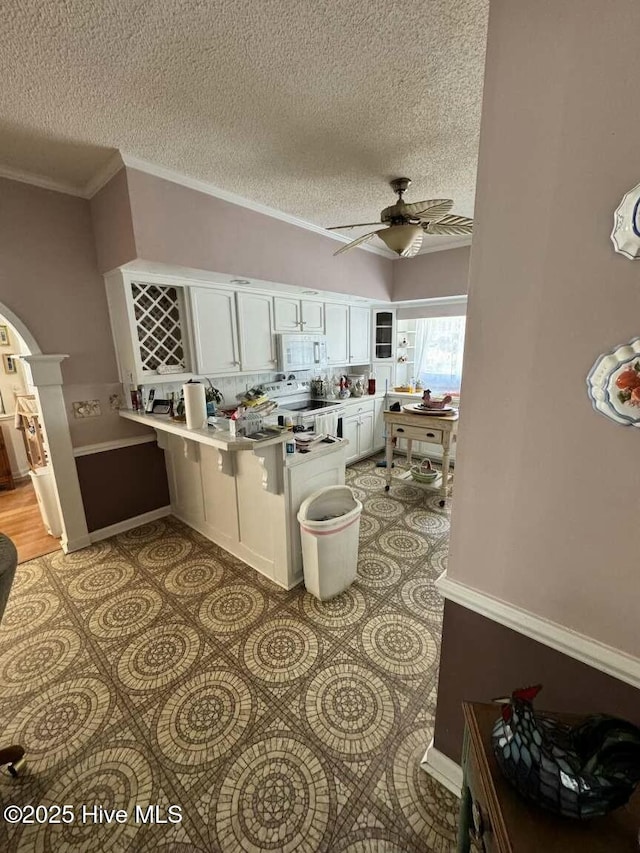 kitchen featuring arched walkways, light tile patterned floors, white microwave, white cabinets, and a peninsula