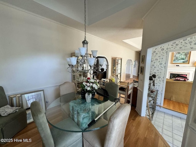 dining space featuring a textured ceiling, light wood-style flooring, a notable chandelier, a fireplace, and vaulted ceiling