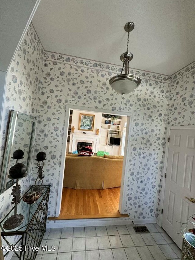 bathroom with a lit fireplace, tile patterned floors, visible vents, and wallpapered walls