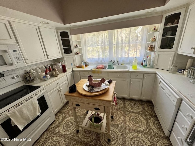 kitchen featuring glass insert cabinets, white appliances, light countertops, and a sink