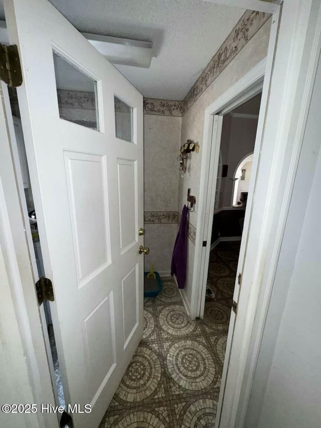 hallway featuring a textured ceiling, light tile patterned floors, and arched walkways