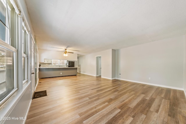 unfurnished living room featuring visible vents, baseboards, light wood finished floors, ceiling fan, and a textured ceiling