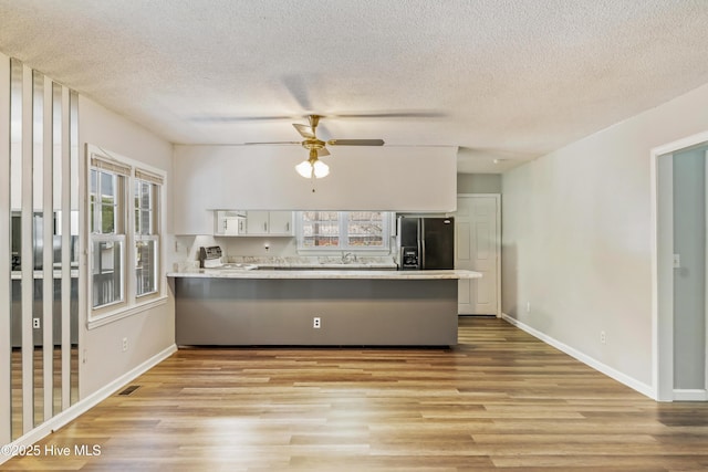 kitchen with a peninsula, electric stove, black fridge with ice dispenser, light wood-style floors, and white cabinetry