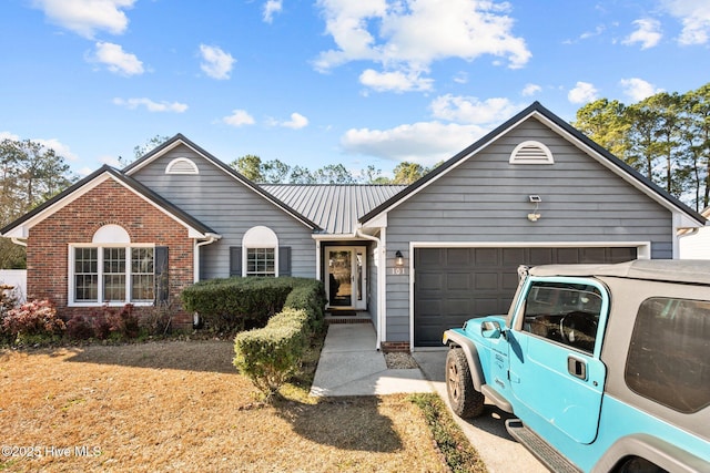 ranch-style house featuring an attached garage, driveway, metal roof, and brick siding