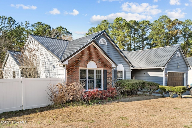 view of front of home with metal roof, an attached garage, brick siding, fence, and a front lawn