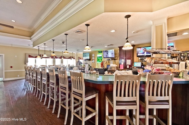 kitchen featuring visible vents, dark wood-style floors, a breakfast bar area, ornamental molding, and hanging light fixtures