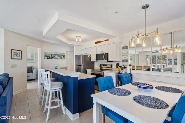 kitchen with a breakfast bar, decorative light fixtures, stainless steel appliances, light countertops, and white cabinetry