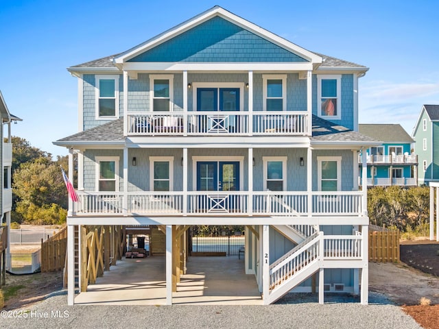 beach home featuring driveway, a shingled roof, stairs, a porch, and a carport