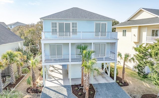 coastal inspired home with a carport, a balcony, driveway, and roof with shingles