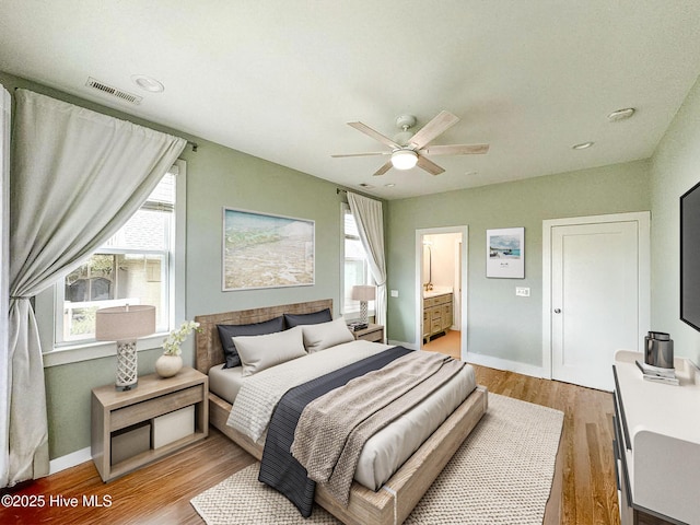 bedroom featuring ceiling fan, ensuite bathroom, visible vents, baseboards, and light wood-style floors