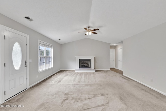 unfurnished living room featuring a fireplace with raised hearth, carpet flooring, visible vents, baseboards, and vaulted ceiling