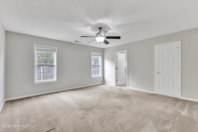 carpeted spare room featuring a textured ceiling, visible vents, a ceiling fan, and baseboards